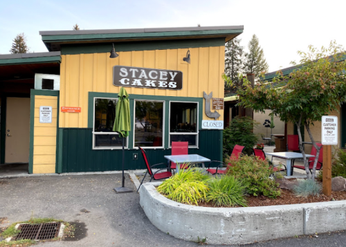 Exterior of Stacey Cakes bakery with a closed sign, outdoor seating, and greenery in front.