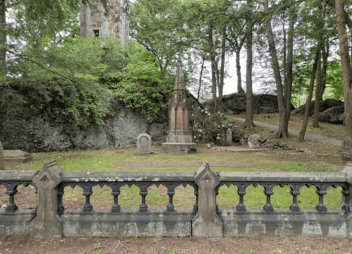 A serene graveyard with a tall, ornate tombstone surrounded by trees and a stone fence.