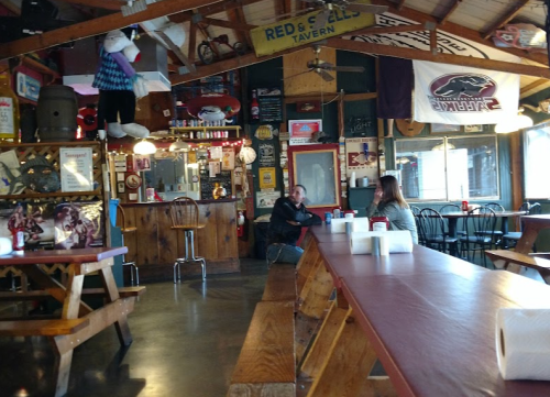 A cozy tavern interior with wooden tables, a bar, and various decorations on the walls, including flags and memorabilia.