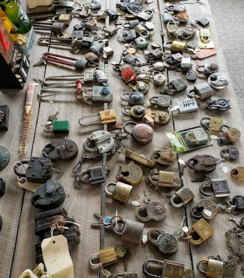 A variety of old locks and padlocks scattered on a wooden table, some with tags and different colors.