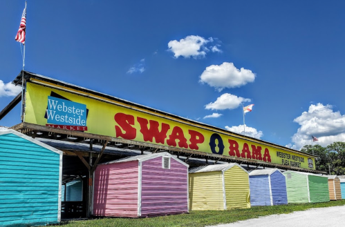 Colorful market stalls under a bright blue sky with clouds, featuring a large "SWAP O RAMA" sign.