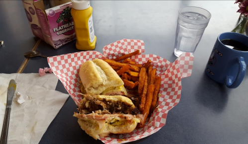 A plate with two sandwiches, sweet potato fries, a glass of water, and a coffee mug on a table.