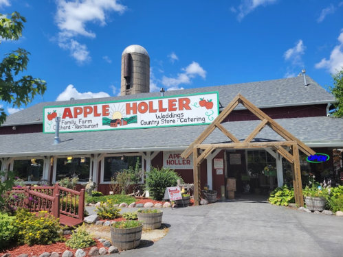 A red barn-style building with a sign reading "Apple Holler" and a wooden entrance, surrounded by greenery and blue skies.