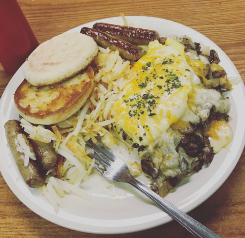 A plate of breakfast food featuring hash browns, sausage links, a biscuit, and a cheesy meat dish topped with herbs.