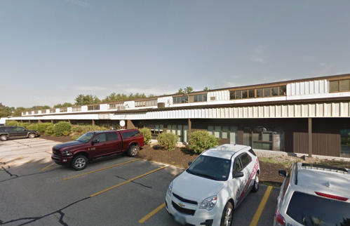 A parking lot with several cars in front of a low-rise commercial building under a clear sky.