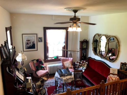 Cozy vintage living room with a red sofa, armchairs, mirrors, and a piano, featuring warm lighting and decorative accents.