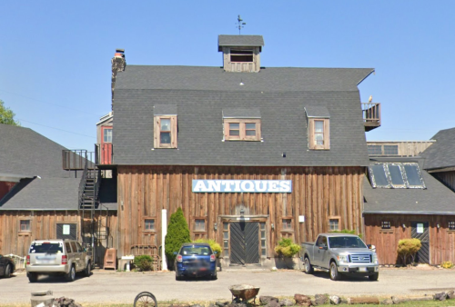 A rustic wooden building with a sign reading "Antiques," featuring multiple windows and a staircase on the side.