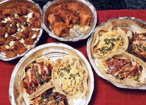 A variety of delicious tacos and appetizers served in aluminum trays on a red cloth.