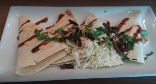 Three tortillas filled with shredded chicken, topped with sauce, cabbage, and herbs, served on a white plate.