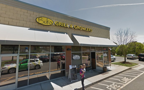 Exterior of Boka Grill & Growlers with a woman standing outside, sunny day, and parked cars in the lot.
