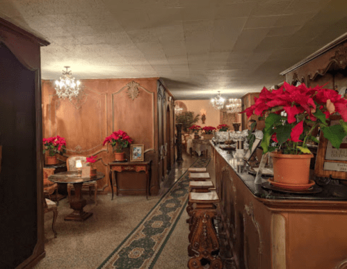 Cozy interior of a restaurant with wooden decor, chandeliers, and festive poinsettias on tables and the bar.