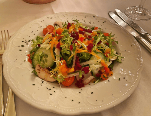 A colorful salad with mixed greens, sliced vegetables, and a sprinkle of herbs on a decorative plate.