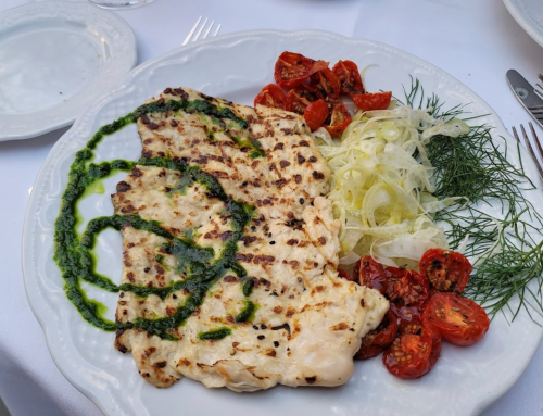 Grilled fish fillet with pesto, served with roasted tomatoes and a side of shredded lettuce and herbs on a white plate.