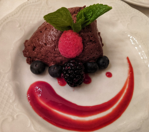 A chocolate mousse dessert garnished with mint, raspberries, blueberries, and a swirl of raspberry sauce on a plate.