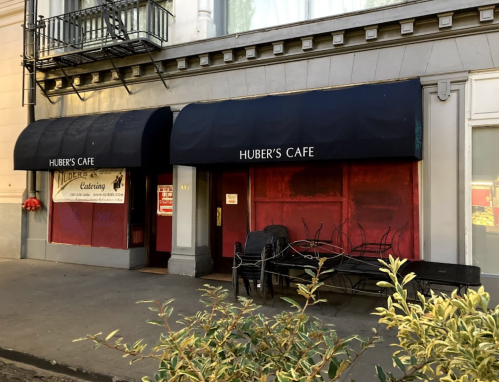 Exterior of Huber's Cafe featuring a dark awning, red walls, and outdoor seating in front.