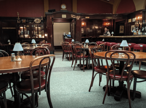A cozy, dimly lit restaurant with wooden tables and chairs, featuring a bar and vintage decor.