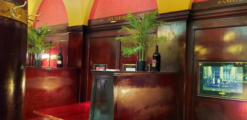 Cozy restaurant interior with dark wood paneling, potted plants, and framed photos on the walls. Warm, inviting atmosphere.