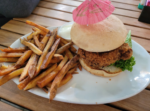 A crispy chicken sandwich with lettuce, served with a side of golden fries and a small cup of dipping sauce.