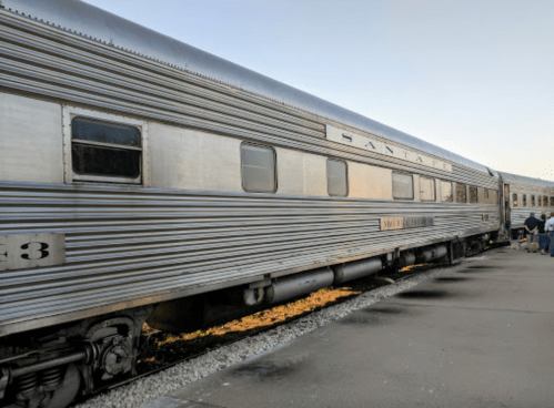 A vintage silver train car parked on a platform, with people nearby and a clear sky in the background.