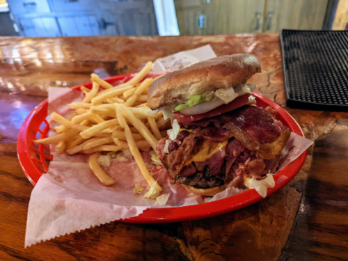 A hearty burger stacked with bacon and cheese, served with a side of crispy French fries in a red basket.