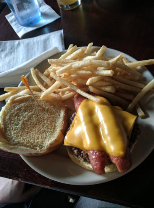 A plate with a cheeseburger topped with a hot dog and a side of golden fries.