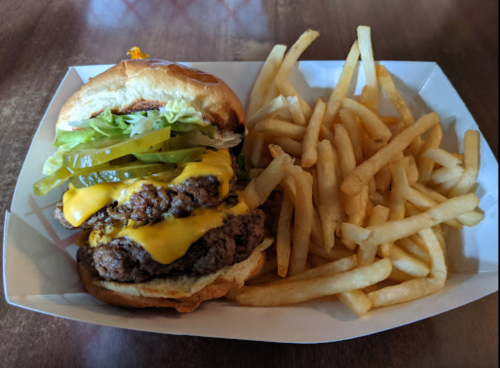 A cheeseburger with lettuce, pickles, and sauce, served with a side of golden French fries in a white tray.
