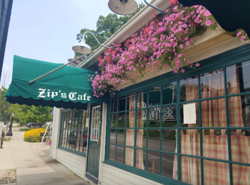 A charming café with a green awning and vibrant flowers, featuring a sign that reads "Zip's Cafe."