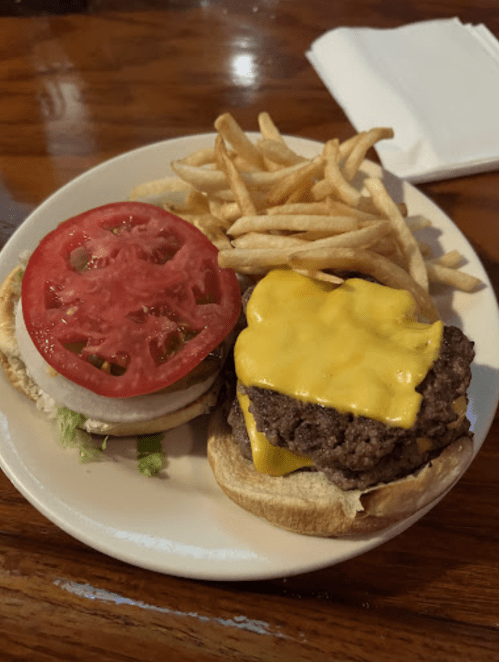 A cheeseburger with melted cheese and tomato on a bun, served with a side of fries on a plate.