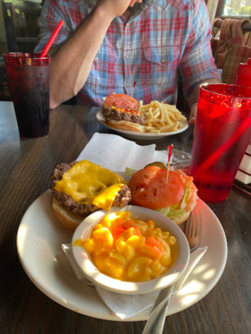 A plate with a cheeseburger, macaroni and cheese, and a side salad, with drinks in red cups in the background.