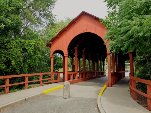A red covered bridge with a wooden walkway, surrounded by greenery and trees.