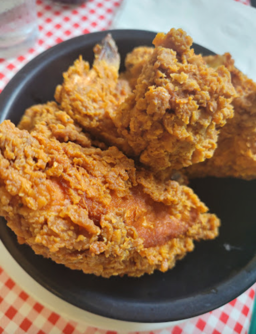 A close-up of crispy fried chicken pieces in a black bowl on a checkered tablecloth.