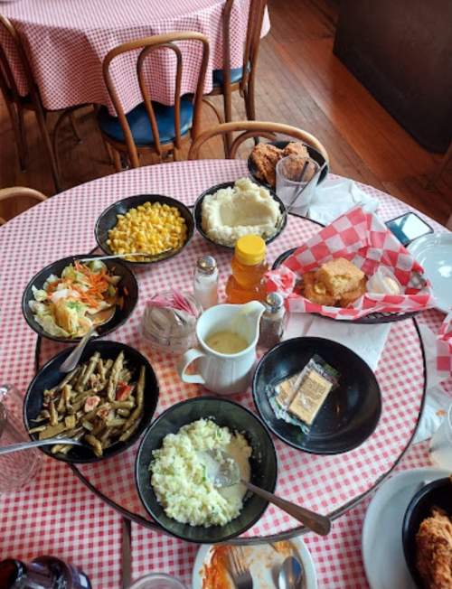 A table set with various Southern dishes, including fried chicken, mac and cheese, salad, and gravy, on a checkered tablecloth.
