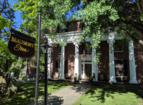 Historic brick building with white columns, surrounded by greenery, featuring a sign that reads "Beaumont Inn."
