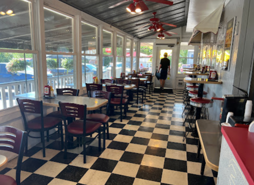 A diner interior with checkered floors, empty tables, and a person walking towards the exit. Bright and airy atmosphere.
