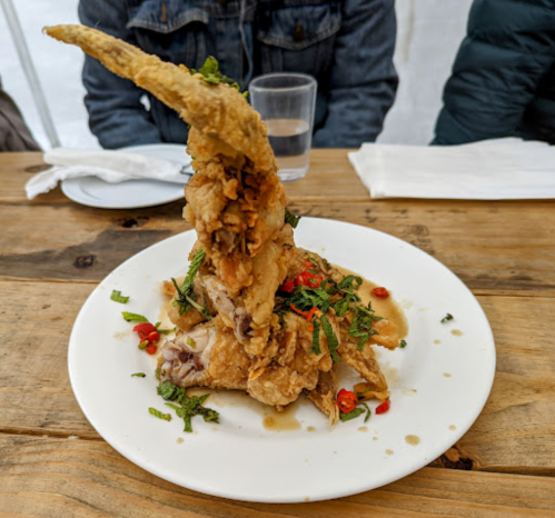 A plate of crispy fried chicken with a tall wing, garnished with herbs and chili, served on a wooden table.