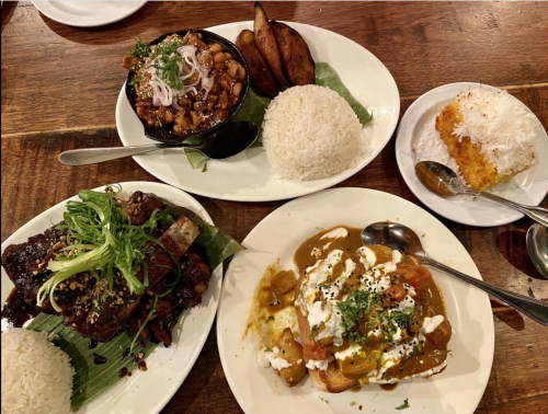 A spread of four dishes: rice, curry, beans, fried plantains, and a dessert, all beautifully presented on white plates.