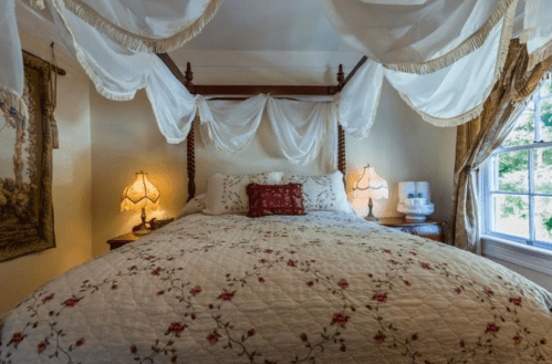 Cozy bedroom with a four-poster bed, floral quilt, draped curtains, and soft lighting from bedside lamps.