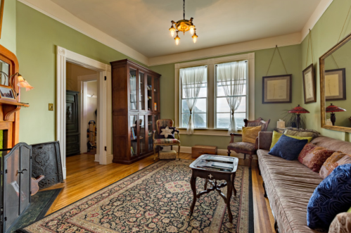 Cozy living room with green walls, a patterned rug, a wooden cabinet, and large windows letting in natural light.