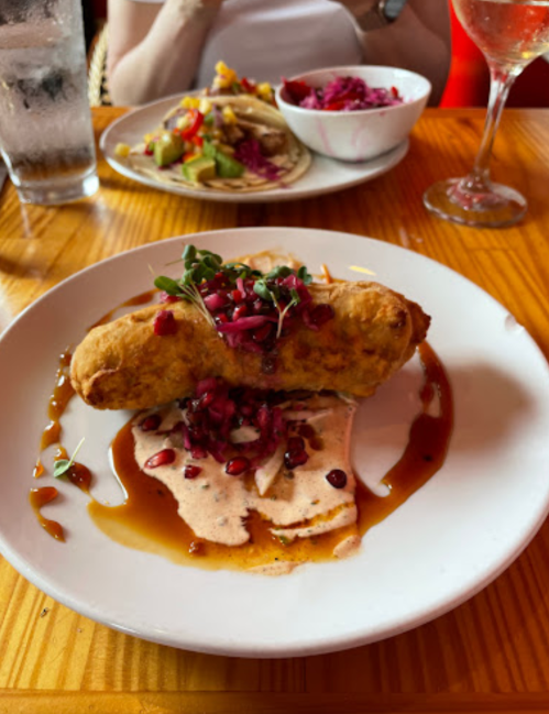 A plate featuring a golden fried dish topped with pomegranate seeds, drizzled with sauce, and served with sides.