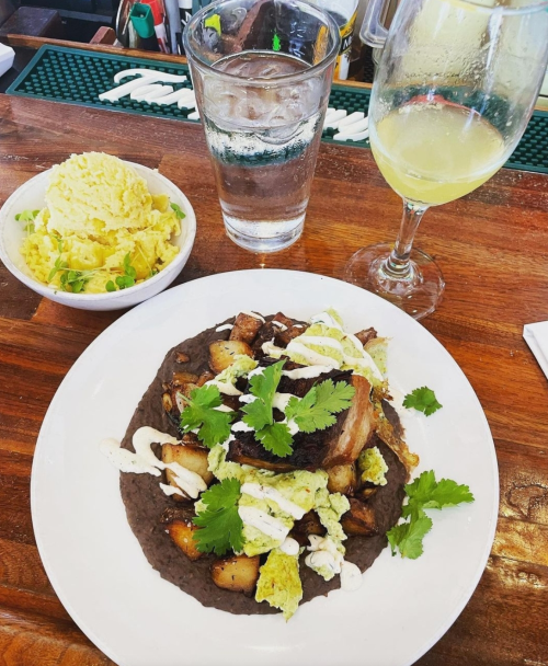 A plate of black beans topped with crispy pork, potatoes, and cilantro, alongside a glass of water and a mimosa.