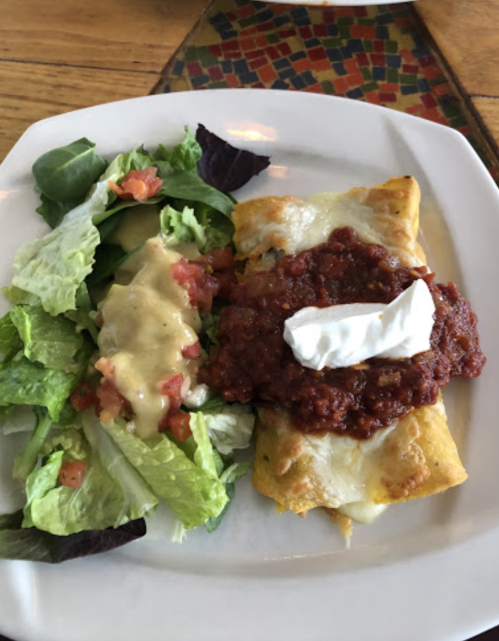 A plate featuring a cheese enchilada topped with salsa and sour cream, alongside a fresh salad with dressing.