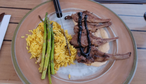 A plate with grilled lamb chops, yellow rice, and asparagus drizzled with sauce.