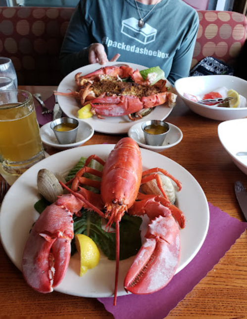 A table setting with two plates of lobster, clams, and lemon, alongside drinks in a casual dining environment.
