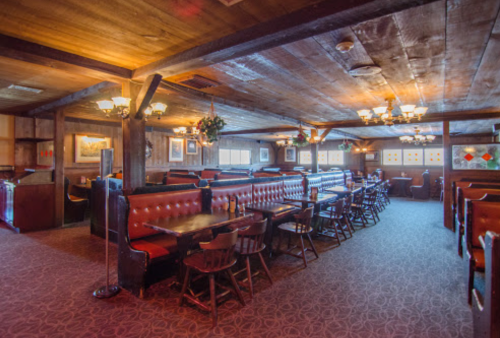 Cozy restaurant interior with wooden beams, booths, and warm lighting, featuring a rustic, inviting atmosphere.