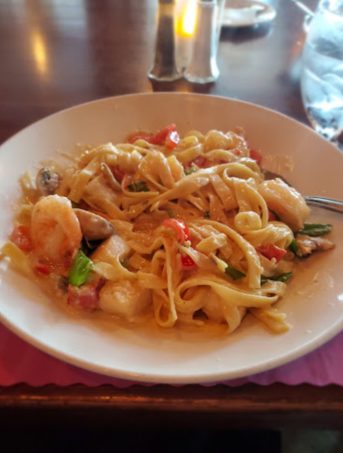 A plate of fettuccine pasta with shrimp, tomatoes, and herbs in a creamy sauce.