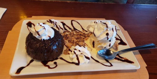 A dessert plate featuring a chocolate lava cake, whipped cream, and vanilla ice cream drizzled with chocolate sauce.