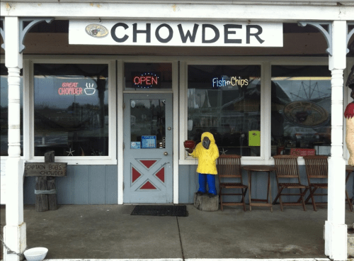 A cozy seafood restaurant entrance with a sign reading "Chowder" and an open neon sign, featuring outdoor seating.