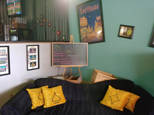 A cozy living room with a black couch, yellow pillows, a chalkboard, and Las Vegas-themed decor on the wall.
