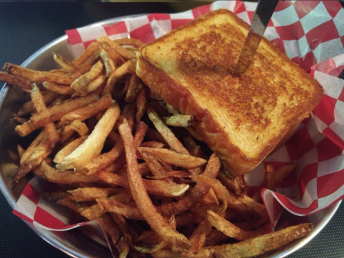 A plate of crispy fries beside a grilled cheese sandwich with a knife inserted, served in a basket with checkered paper.