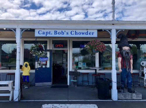 Exterior of Capt. Bob's Chowder, featuring a sign, open door, and a whimsical statue outside. Bright, cloudy sky above.